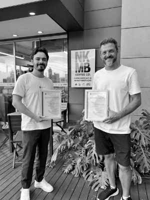 Os sócios da NKMB Coffee Co. segurando os certificados de registro da marca em frente à cafeteria